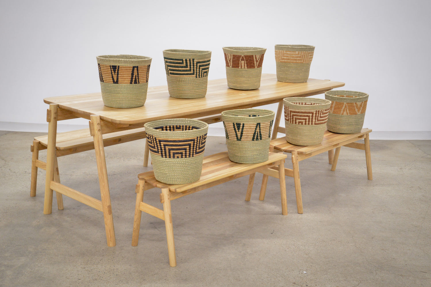 Lightwood dining table and benches showcasing artisan woven baskets with intricate geometric patterns in natural and dyed tones, set against a minimalist background.
