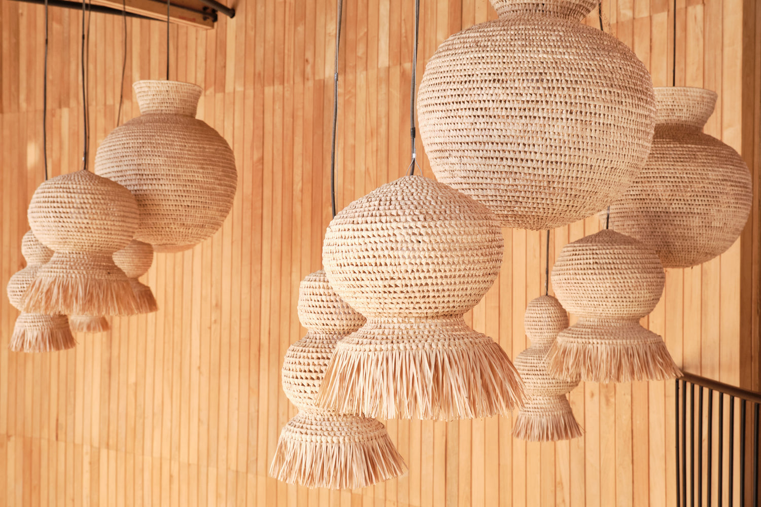 Hanging natural fiber pendant lights with intricate weaves and layered textures, set against a wooden slatted wall, creating a warm and organic ambiance.