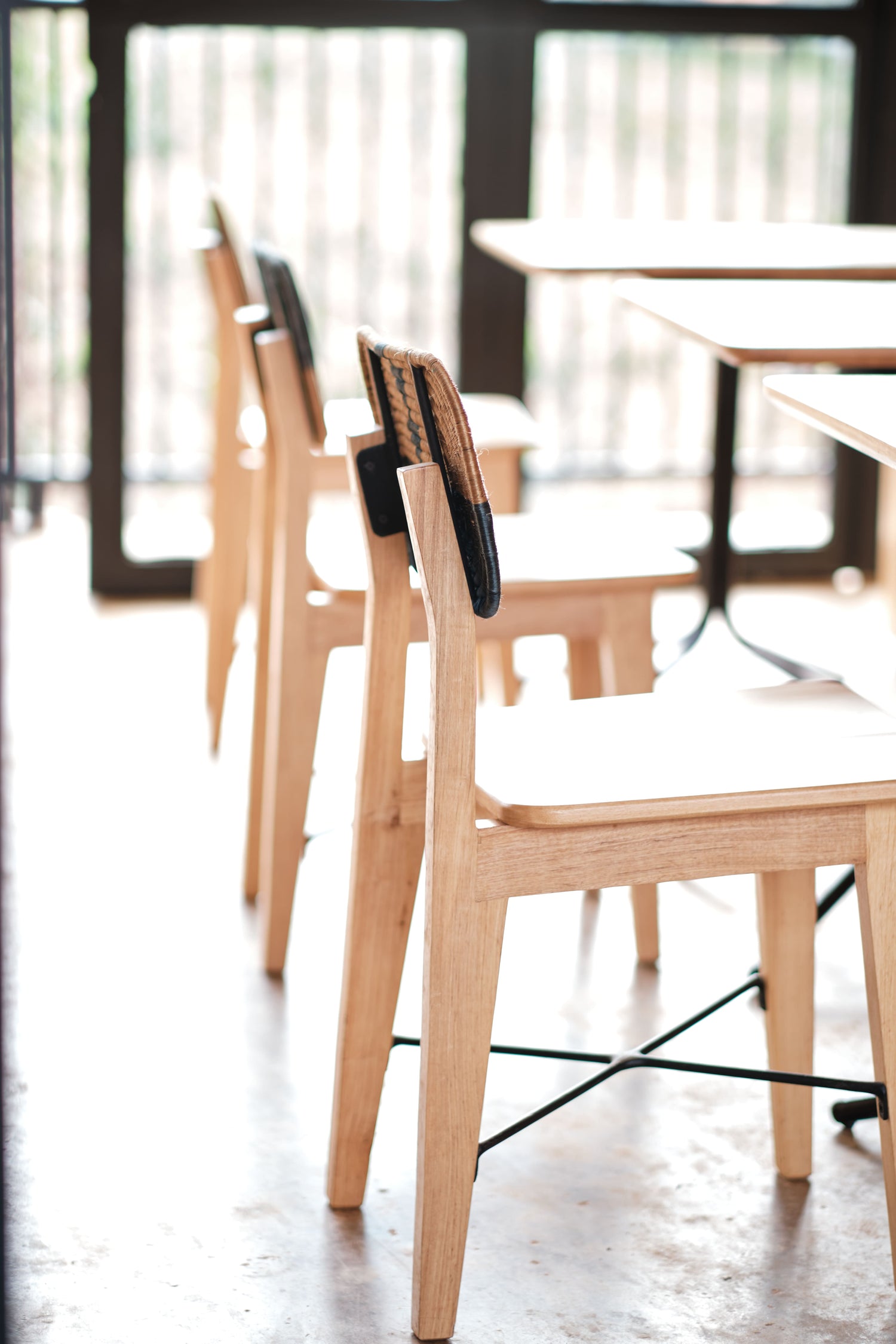 Close-up of lightwood dining chairs with woven backrests, positioned in a sunlit dining area, highlighting the craftsmanship and clean design.